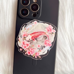 May include: A phone case with a pink and white floral design featuring a red and white koi fish swimming in a circle.