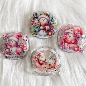 May include: Four round, clear, glass ornaments with a winter theme. Each ornament features a different snowman design with a pink, white, and red color scheme. The ornaments have glitter and a 3D effect. The text "Merry and Bright" is on one ornament.