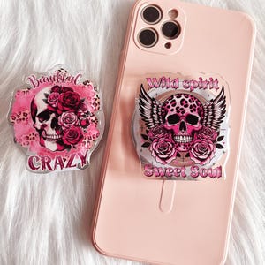 May include: Two phone grips with a pink and black skull design. One grip says "Beautiful Crazy" and the other says "Wild Spirit Sweet Soul".