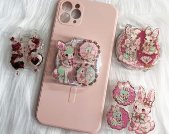 May include: A pink phone case with a pop socket featuring a deer and bunny design. Several decorative resin pieces with bunny and deer motifs are scattered around the phone case, showcasing a pastel colour palette.
