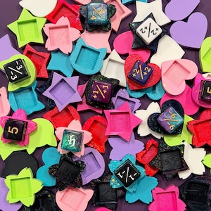 May include: A collection of colorful, geometric dice and decorative shapes in various colors, including pink, purple, green, and blue. The dice feature numbers and fractions. The shapes include stars, hearts, and squares.