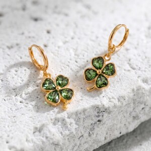 Peut inclure: Une paire de boucles d'oreilles cr&eacute;oles dor&eacute;es avec des pendentifs en forme de tr&egrave;fle &agrave; quatre feuilles. Chaque tr&egrave;fle est compos&eacute; de quatre p&eacute;tales en cristal vert olive facett&eacute;, sertis dans une monture en m&eacute;tal dor&eacute; brillant.