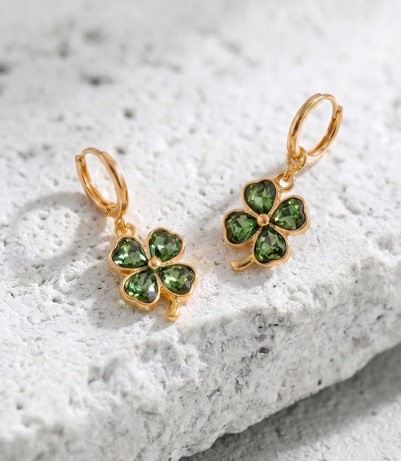 Peut inclure: Une paire de boucles d'oreilles cr&eacute;oles dor&eacute;es avec des pendentifs en forme de tr&egrave;fle &agrave; quatre feuilles. Chaque tr&egrave;fle est compos&eacute; de quatre p&eacute;tales en cristal vert olive facett&eacute;, sertis dans une monture en m&eacute;tal dor&eacute; brillant.