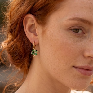 Peut inclure: Une boucle d'oreille cr&eacute;ole en or avec un petit pendentif en forme de tr&egrave;fle &agrave; quatre feuilles dot&eacute; d'une finition en &eacute;mail vert vif. Le tr&egrave;fle pr&eacute;sente un contour dor&eacute; m&eacute;tallique et un d&eacute;tail central dor&eacute;, suspendu &agrave; un anneau simple en or.