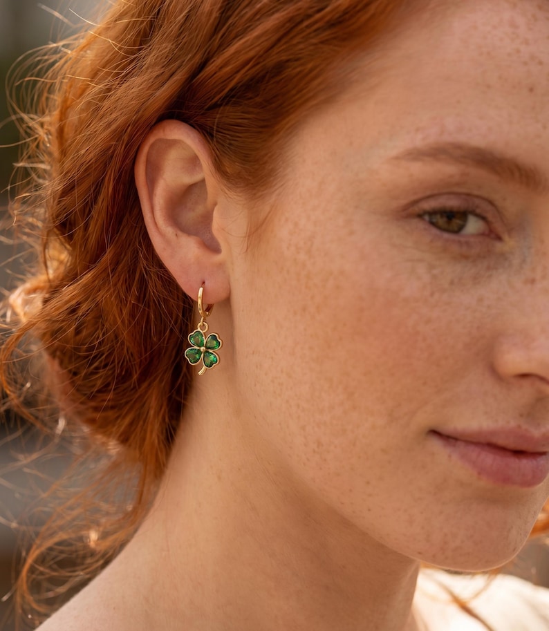Peut inclure: Une boucle d'oreille cr&eacute;ole en or avec un petit pendentif en forme de tr&egrave;fle &agrave; quatre feuilles dot&eacute; d'une finition en &eacute;mail vert vif. Le tr&egrave;fle pr&eacute;sente un contour dor&eacute; m&eacute;tallique et un d&eacute;tail central dor&eacute;, suspendu &agrave; un anneau simple en or.