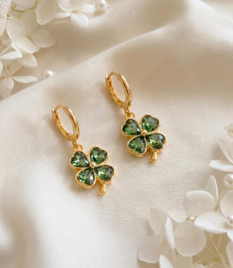 Peut inclure: Une paire de boucles d'oreilles cr&eacute;oles dor&eacute;es avec des pendentifs en forme de tr&egrave;fle &agrave; quatre feuilles. Chaque tr&egrave;fle est compos&eacute; de quatre p&eacute;tales en cristal vert fonc&eacute; taill&eacute;s en forme de c&oelig;ur, sertis dans une monture en m&eacute;tal dor&eacute;.