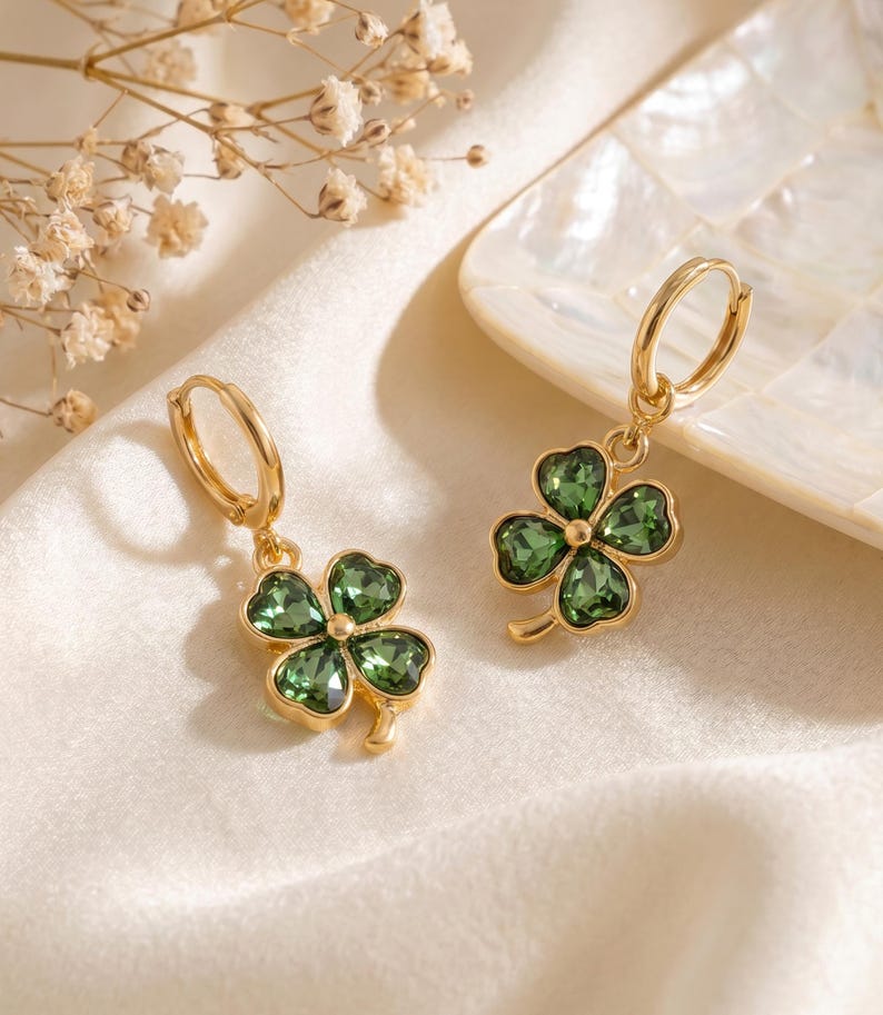 Peut inclure: Une paire de boucles d'oreilles cr&eacute;oles dor&eacute;es avec des pendentifs en forme de tr&egrave;fle &agrave; quatre feuilles. Chaque tr&egrave;fle est compos&eacute; de quatre cristaux vert fonc&eacute; facett&eacute;s sertis dans une monture en m&eacute;tal dor&eacute;, suspendus &agrave; une cr&eacute;ole simple.
