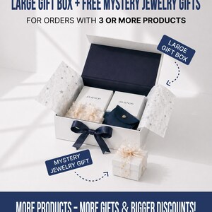Op de afbeelding: Een witte geschenkdoos met een marineblauw interieur en strik, met sieradendoosjes en een klein zakje. De tekst luidt "LARGE GIFT BOX + FREE MYSTERY JEWELRY GIFTS" en "MORE PRODUCTS - MORE GIFTS & BIGGER DISCOUNTS!"