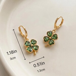 Peut inclure: Une paire de boucles d'oreilles cr&eacute;oles dor&eacute;es avec des pendentifs tr&egrave;fles &agrave; quatre feuilles orn&eacute;s de cristaux verts. Les boucles mesurent 3 cm de longueur totale et 1,3 cm de largeur. Les tr&egrave;fles sont en m&eacute;tal dor&eacute; avec des pierres vertes facett&eacute;es.