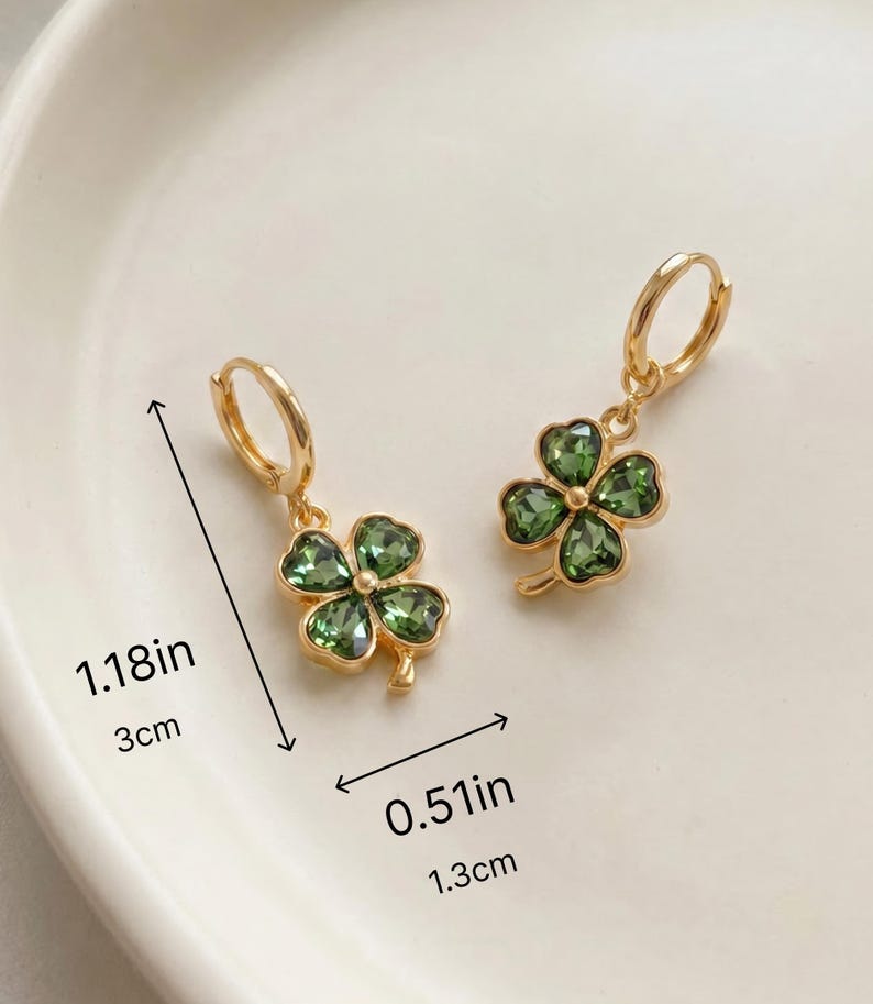 Peut inclure: Une paire de boucles d'oreilles cr&eacute;oles dor&eacute;es avec des pendentifs tr&egrave;fles &agrave; quatre feuilles orn&eacute;s de cristaux verts. Les boucles mesurent 3 cm de longueur totale et 1,3 cm de largeur. Les tr&egrave;fles sont en m&eacute;tal dor&eacute; avec des pierres vertes facett&eacute;es.