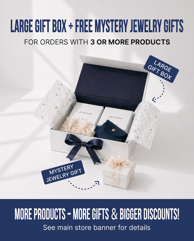 May include: A white rectangular gift box with a dark blue ribbon, containing two white boxes labeled JOLIS NOR, a dark blue pouch, and star-patterned tissue paper. A smaller white gift box sits in front with text labels Large Gift Box and Mystery Jewelry Gift.