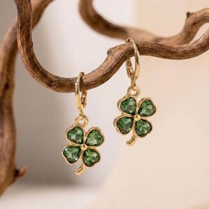 Peut inclure: Une paire de boucles d'oreilles cr&eacute;oles dor&eacute;es avec des pendentifs en forme de tr&egrave;fle &agrave; quatre feuilles. Chaque tr&egrave;fle est compos&eacute; de quatre p&eacute;tales en cristal vert fonc&eacute; facett&eacute;, sertis dans une monture en m&eacute;tal dor&eacute; poli.