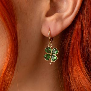 Peut inclure: Une boucle d'oreille cr&eacute;ole dor&eacute;e orn&eacute;e d'un pendentif en forme de tr&egrave;fle &agrave; quatre feuilles. Le pendentif est compos&eacute; d'un contour en m&eacute;tal dor&eacute; poli et rempli d'&eacute;mail vert translucide, offrant une finition brillante et lumineuse.