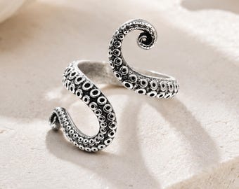 May include: A silver-toned open ring shaped like an octopus tentacle, featuring a textured surface with numerous circular suction cups. The metal has a darkened, oxidized finish in the recessed areas to highlight the detailed suckers.