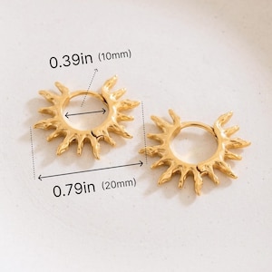 Op de afbeelding: Een paar goudkleurige oorringen met een zonnestraalontwerp. De binnendiameter is 10 mm en de totale buitendiameter is 20 mm. De oorbellen hebben getextureerde, onregelmatige stralen die uitsteken vanaf het ronde frame van de ring.