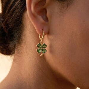 Peut inclure: Une boucle d'oreille cr&eacute;ole dor&eacute;e avec un pendentif en forme de tr&egrave;fle &agrave; quatre feuilles. Le tr&egrave;fle se compose de quatre pierres vertes translucides en forme de c&oelig;ur serties dans une monture dor&eacute;e, avec une petite tige dor&eacute;e &agrave; la base.