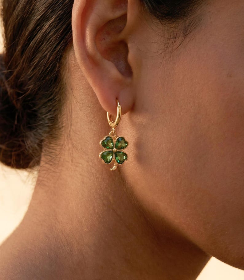Peut inclure: Une boucle d'oreille cr&eacute;ole dor&eacute;e avec un pendentif en forme de tr&egrave;fle &agrave; quatre feuilles. Le tr&egrave;fle se compose de quatre pierres vertes translucides en forme de c&oelig;ur serties dans une monture dor&eacute;e, avec une petite tige dor&eacute;e &agrave; la base.