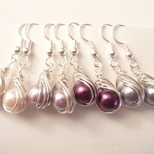 May include: Six pairs of silver wire wrapped earrings with pearl-like beads in shades of pink, purple, and gray.