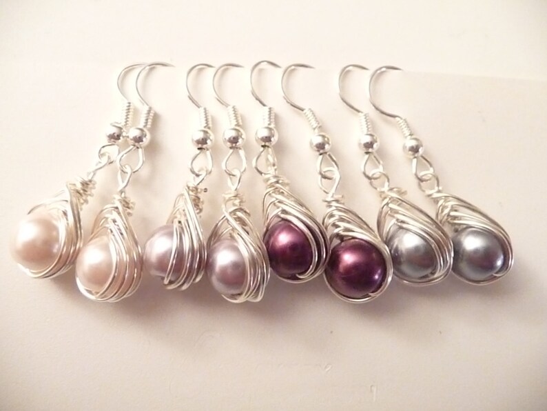 May include: Six pairs of silver wire wrapped earrings with pearl-like beads in shades of pink, purple, and gray.