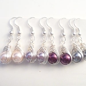 May include: Six pairs of silver wire wrapped earrings with pearl accents. The pearls are in shades of pink, purple, and gray.