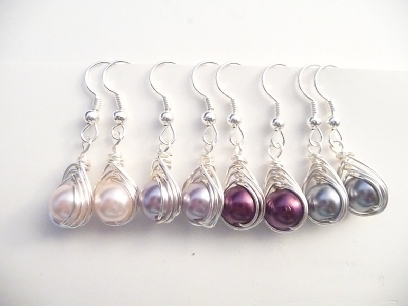 May include: Six pairs of silver wire wrapped earrings with pearl accents. The pearls are in shades of pink, purple, and gray.