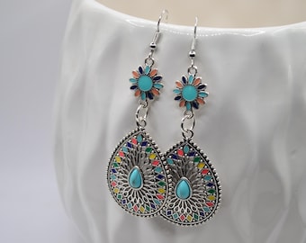 May include: Silver-toned dangle earrings with a floral top and teardrop-shaped bottom. The earrings feature turquoise, orange, blue, and yellow accents. The teardrop design has a filigree pattern and a turquoise stone in the center.