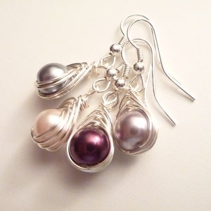 May include: A set of three silver wire wrapped pearl earrings. The pearls are in shades of gray, pink, and purple.