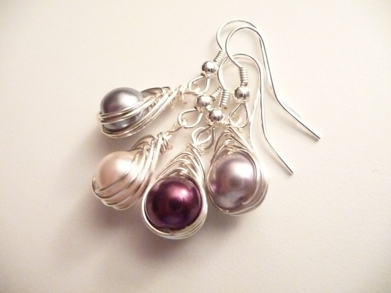May include: A set of three silver wire wrapped pearl earrings. The pearls are in shades of gray, pink, and purple.