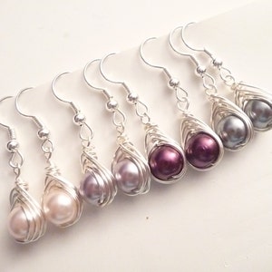 May include: Six pairs of silver wire wrapped earrings with pearl drops in various shades of purple, pink, and gray.