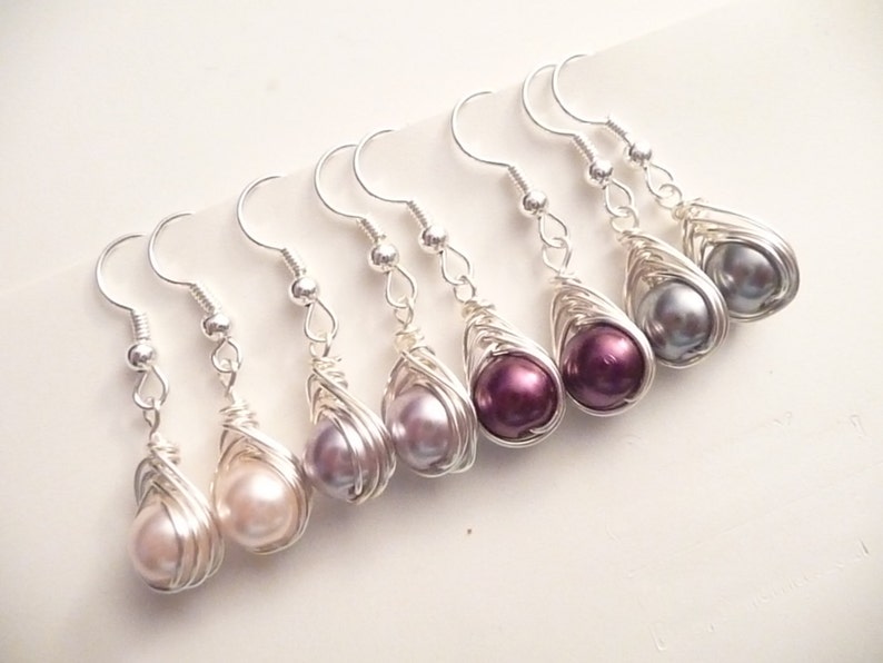 May include: Six pairs of silver wire wrapped earrings with pearl drops in various shades of purple, pink, and gray.