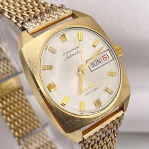 May include: A gold-tone Longines Admiral Automatic watch with a white dial, gold hour markers, and a mesh metal strap. The dial features the text Longines, Automatic, and ADMIRAL with five stars, plus a day-date window displaying SUN 6.