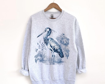 May include: A grey sweatshirt featuring a blue heron illustration on the front. The heron is standing in a blue and white watercolour-style background.