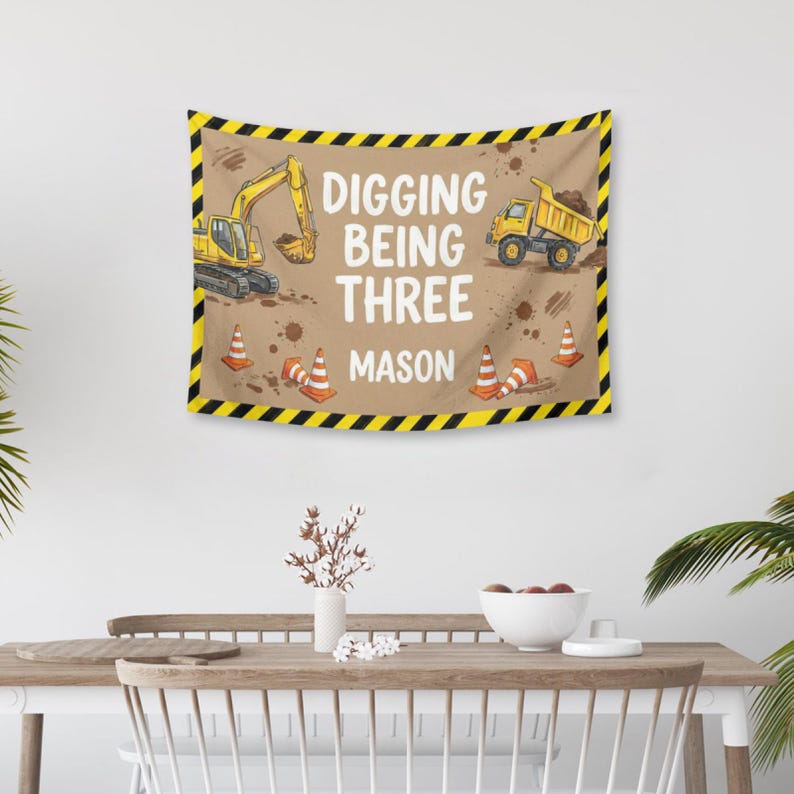 Puede incluir: Un tapiz marr&oacute;n con un tema de construcci&oacute;n, con una excavadora y un cami&oacute;n volquete amarillos. El texto "Digging Being Three Mason" se muestra en blanco. El borde es de rayas negras y amarillas, con conos de tr&aacute;fico naranjas.
