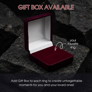 Op de afbeelding: Een open, bordeauxrode fluwelen ringdoos, ideaal om een ring te presenteren. De doos staat tegen een donkere, getextureerde achtergrond. Tekst luidt "GIFT BOX AVAILABLE" en "your favorite ring". De tekst onderaan luidt "Add Gift Box to each ring to create unforgettable moments for you and your loved ones!"