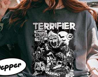 May include: Dark gray t-shirt with the word "TERRIFIER" in white block letters. The shirt features a black and white graphic of a scary clown and the text "CHAOS! VIOLENCE! CORE!" and "WARNING! THIS FILM IS NOT SUITABLE FOR THE FAINT OF HEART".