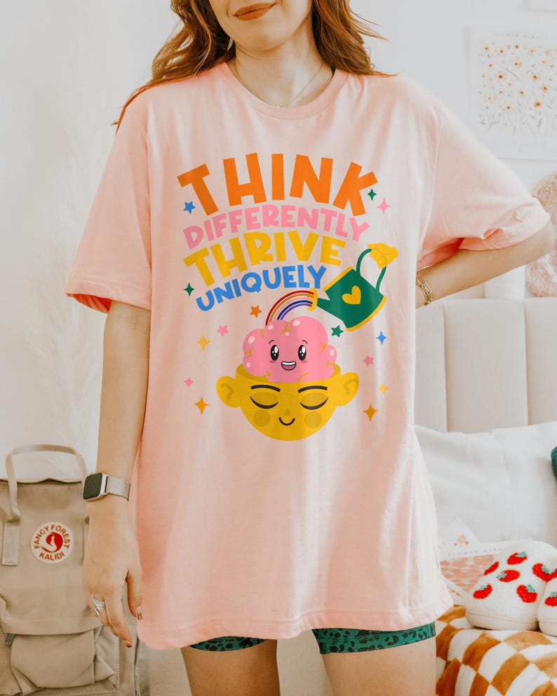 Autism Shirt with a positive message: 'Think Differently, Thrive Uniquely.' This Autism Awareness Shirt features a colorful design with a smiling brain, rainbow, and watering can, symbolizing growth and neurodiversity. Perfect as an Autism Teacher Shirt, Neurodivergent Shirt, ADHD Shirt, Anxiety Shirt, or ABA Therapist Shirt to promote inclusivity and self-expression