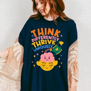 Autism Shirt with a positive message: 'Think Differently, Thrive Uniquely.' This Autism Awareness Shirt features a colorful design with a smiling brain, rainbow, and watering can, symbolizing growth and neurodiversity. Perfect as an Autism Teacher Shirt, Neurodivergent Shirt, ADHD Shirt, Anxiety Shirt, or ABA Therapist Shirt to promote inclusivity and self-expression