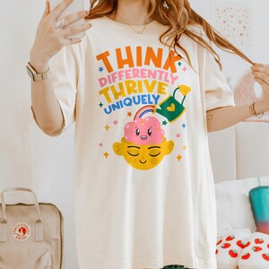 Autism Shirt with a positive message: 'Think Differently, Thrive Uniquely.' This Autism Awareness Shirt features a colorful design with a smiling brain, rainbow, and watering can, symbolizing growth and neurodiversity. Perfect as an Autism Teacher Shirt, Neurodivergent Shirt, ADHD Shirt, Anxiety Shirt, or ABA Therapist Shirt to promote inclusivity and self-expression