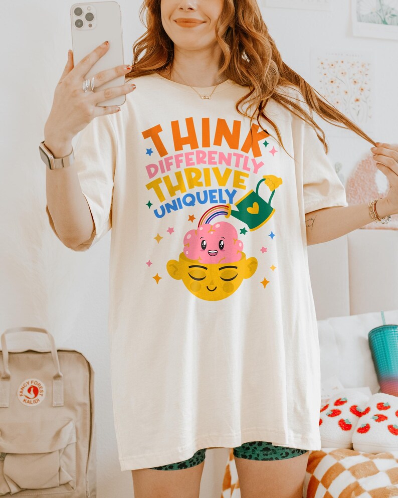 Autism Shirt with a positive message: 'Think Differently, Thrive Uniquely.' This Autism Awareness Shirt features a colorful design with a smiling brain, rainbow, and watering can, symbolizing growth and neurodiversity. Perfect as an Autism Teacher Shirt, Neurodivergent Shirt, ADHD Shirt, Anxiety Shirt, or ABA Therapist Shirt to promote inclusivity and self-expression