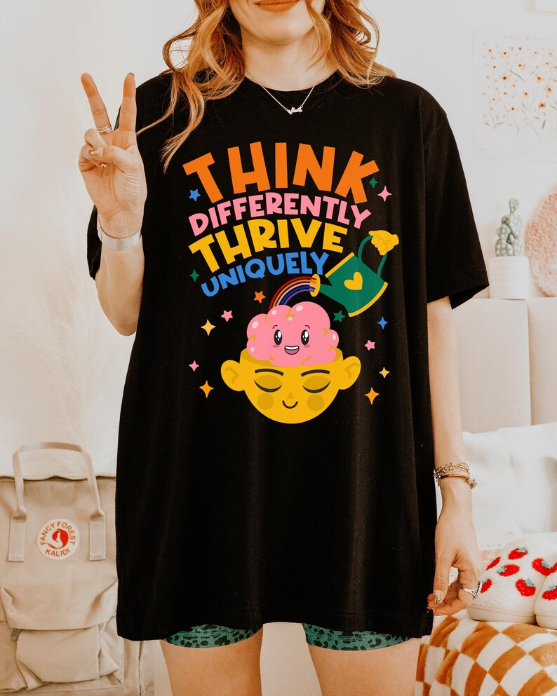Autism Shirt with a positive message: 'Think Differently, Thrive Uniquely.' This Autism Awareness Shirt features a colorful design with a smiling brain, rainbow, and watering can, symbolizing growth and neurodiversity. Perfect as an Autism Teacher Shirt, Neurodivergent Shirt, ADHD Shirt, Anxiety Shirt, or ABA Therapist Shirt to promote inclusivity and self-expression