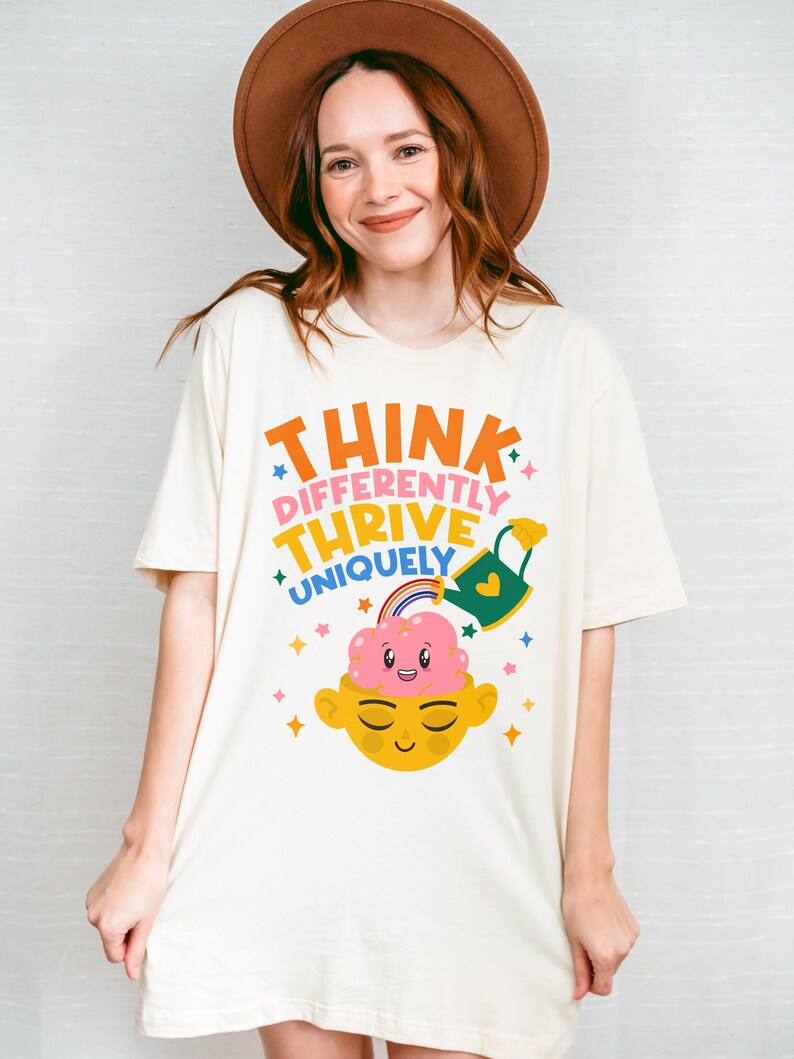 Autism Shirt with a positive message: 'Think Differently, Thrive Uniquely.' This Autism Awareness Shirt features a colorful design with a smiling brain, rainbow, and watering can, symbolizing growth and neurodiversity. Perfect as an Autism Teacher Shirt, Neurodivergent Shirt, ADHD Shirt, Anxiety Shirt, or ABA Therapist Shirt to promote inclusivity and self-expression