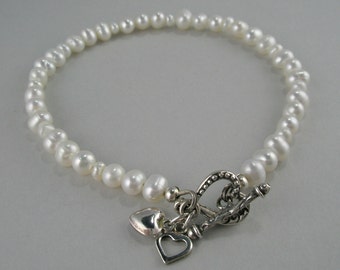 May include: A white pearl bracelet with a silver heart-shaped clasp. The bracelet is made of small, round pearls and has a delicate, feminine look.