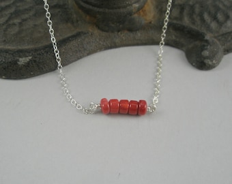 Op de afbeelding: Een zilveren ketting met een rij kleine, rode koraal kralen.