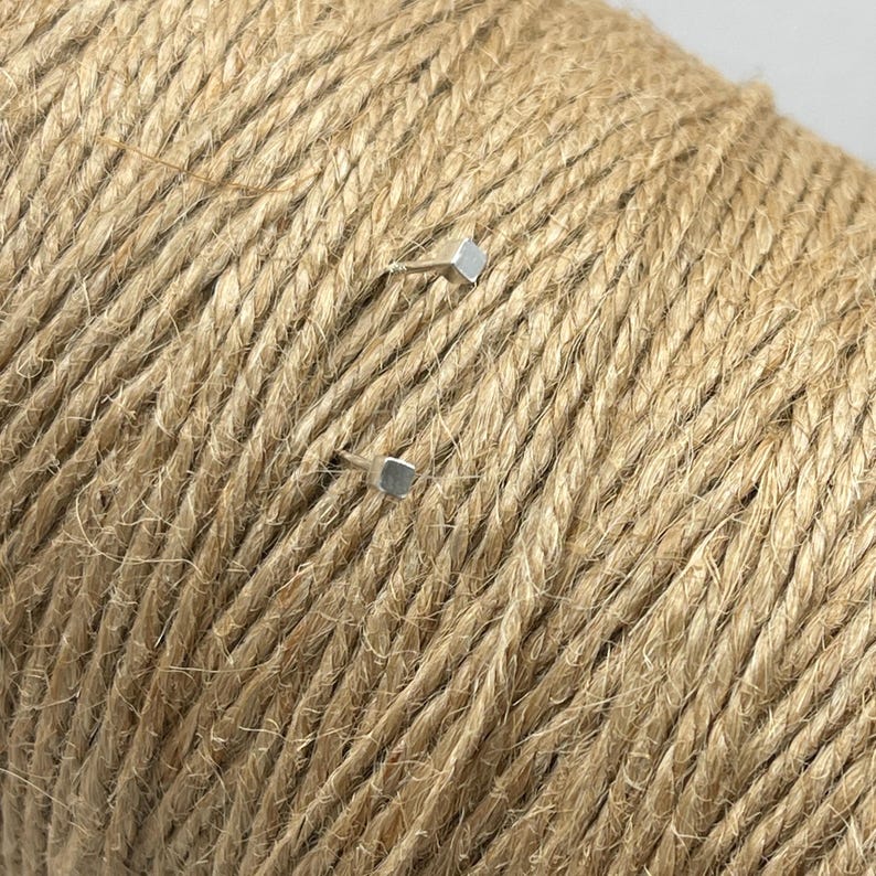 May include: Two silver square-shaped push pins are stuck into a roll of natural brown twine.