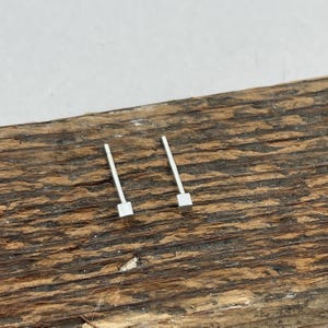 May include: A pair of silver square stud earrings on a wooden surface.