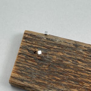 May include: A pair of small, silver square stud earrings on a piece of weathered wood.