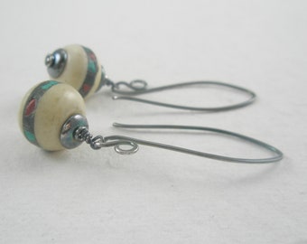 Op de afbeelding: Een paar oorhangers met witte en turquoise gepatroneerde kralen en zilveren draadhaken.