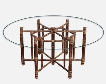 Pode incluir: Uma mesa redonda com tampo de vidro e estrutura de bambu marrom. A mesa tem um design único e intrincado com múltiplos apoios em forma de cruz.