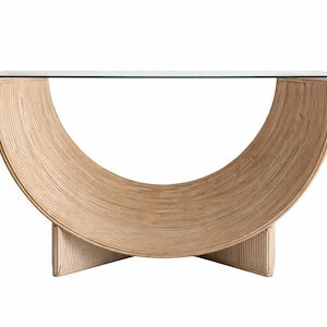 Puede incluir: Una consola moderna con una tapa de vidrio transparente y una base curva en forma de media luna hecha de ratán tejido de color claro. La base está soportada por dos patas en forma de cruz, creando un mueble elegante y funcional.