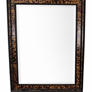 May include: Rectangular mirror with a black frame and a decorative tortoiseshell pattern. The mirror's frame has a double border design, adding depth and visual interest. The tortoiseshell pattern features shades of brown and black.